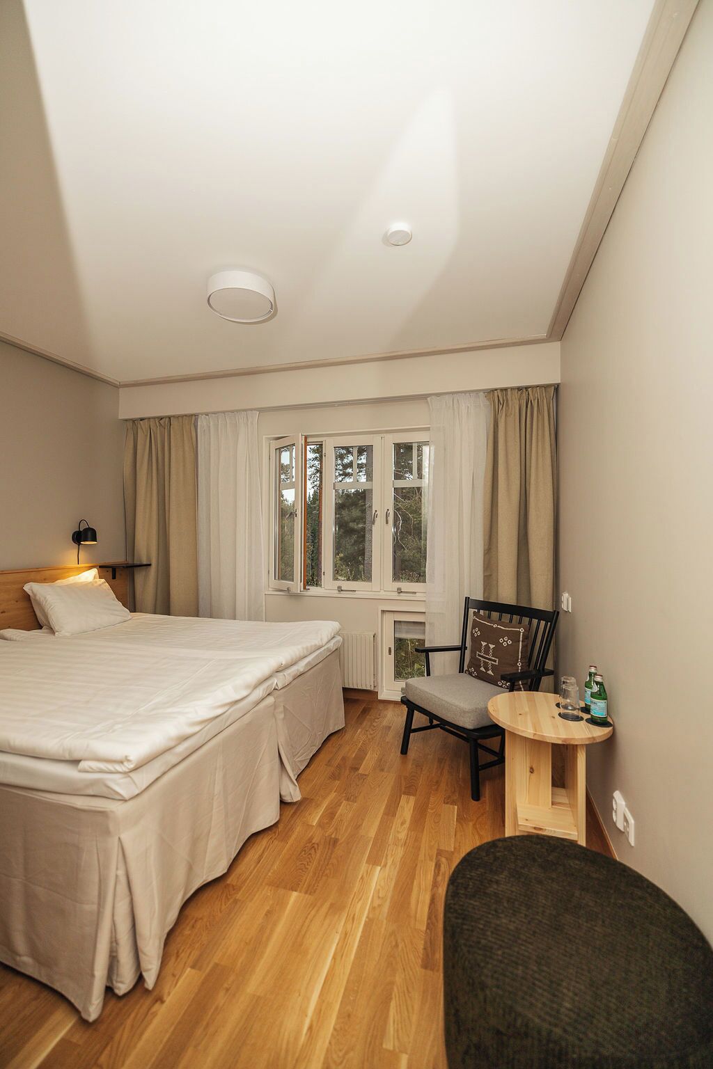 Een slaapkamer met een bed, een stoel, een tafeltje en een raam met gordijnen.
