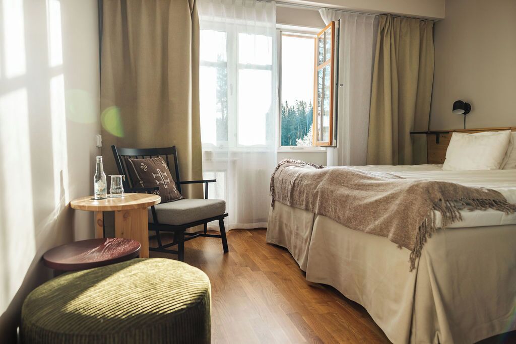 Una habitación de hotel con una cama, una silla, una mesita y una ventana con cortinas.