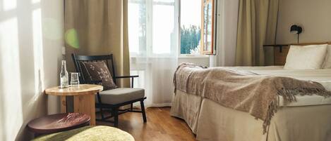Una habitación de hotel con una cama, una silla, una mesita y una ventana con cortinas.