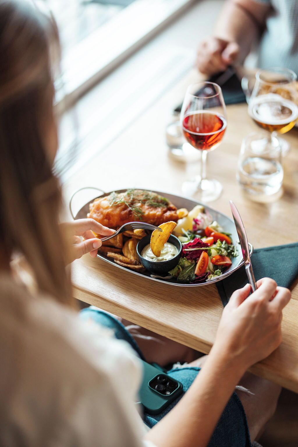 A dining table with a plate of food, a glass of red wine, and a smartphone.