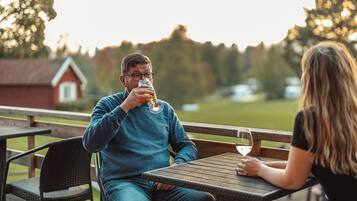 Två personer sitter vid ett bord utomhus, och på bordet står ett glas vin, ett glas öl och en ölflaska.