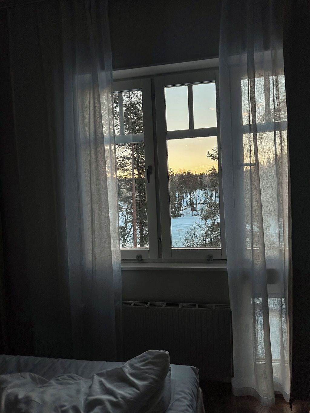 A bedroom with a large window, a radiator below, and a bed with a white cover.