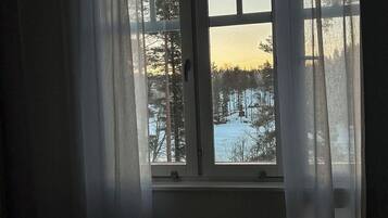 Ett sovrum med ett stort fönster, ett element under fönstret och en säng med ett vitt överkast.