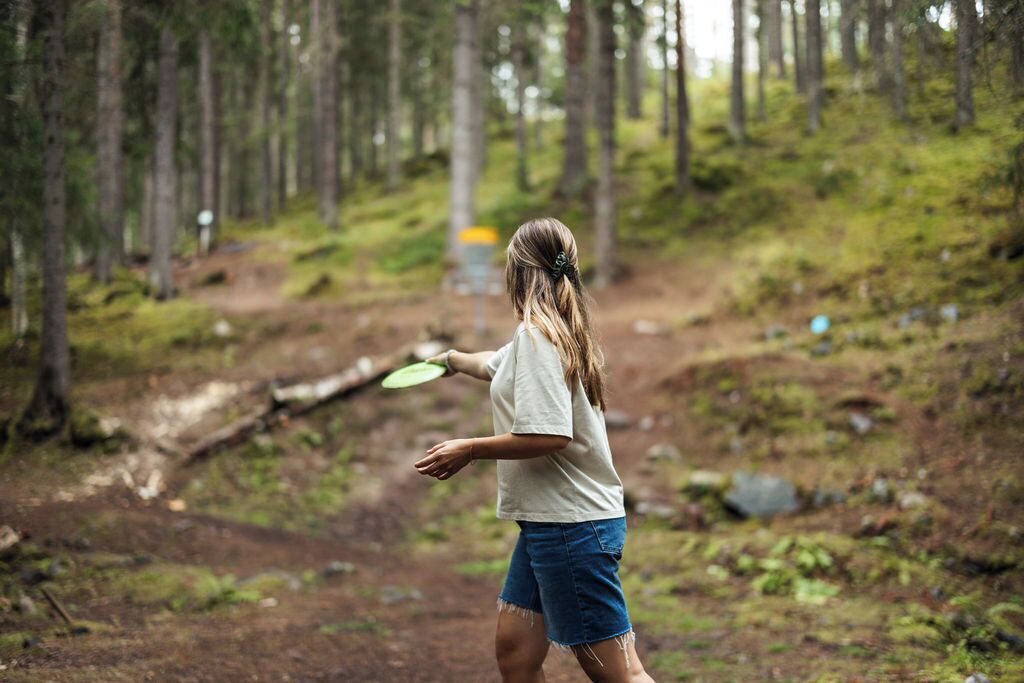 A person walking in a forested area with a frisbee.