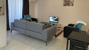 Ein modernes Wohnzimmer mit grauem Sofa, einem kleinen Tisch, einem Fernseher und einer Deckenleuchte.