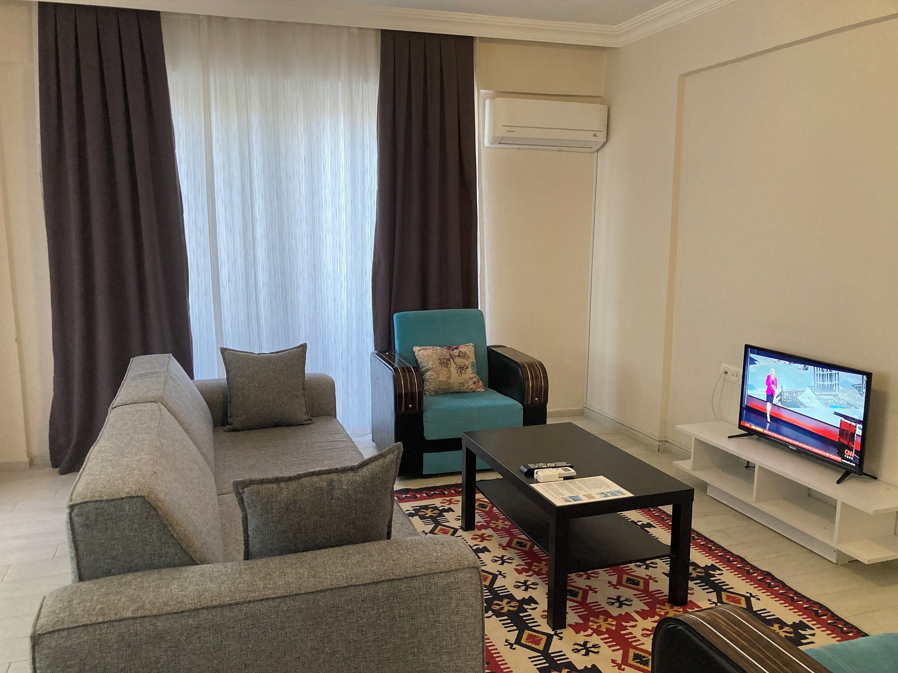 Una sala de estar con un sofá, un sillón azul, una mesa de centro y una televisión.