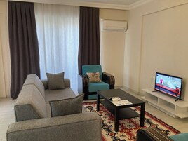 Una sala de estar con un sofá, un sillón azul, una mesa de centro y una televisión.