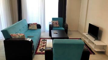 Una sala de estar con sofá, sillón, mesa de centro, televisor y alfombra.