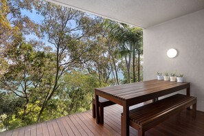 Eine Holzterrasse mit Tisch und Bank bietet einen schönen Blick auf Bäume und ein Gewässer.