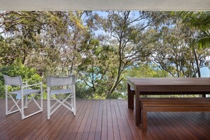Una terraza de madera con una silla metálica blanca y una mesa de madera.