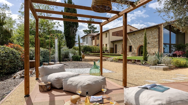 A wooden pergola with a table set for a meal, outdoor seating, and a stone building in the background.