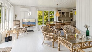 Amplia sala de estar con mobiliario de mimbre, una mesa de centro de vidrio y un televisor sobre un mueble.