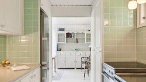 Cocina estrecha con armarios blancos, horno empotrado y encimera con una tetera y un cuaderno.