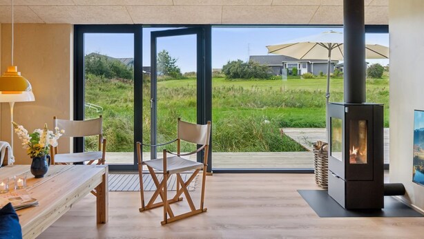 A modern living room with a large glass door leading to a grassy outdoor area, a wood-burning stove, and a dining table with chairs. - "Aatos" - 250m from the sea by Interhome (Knebel)