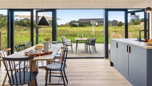 A modern kitchen with large windows, a dining area with wooden furniture, and a view of a green landscape. - "Aatos" - 250m from the sea by Interhome (Knebel)