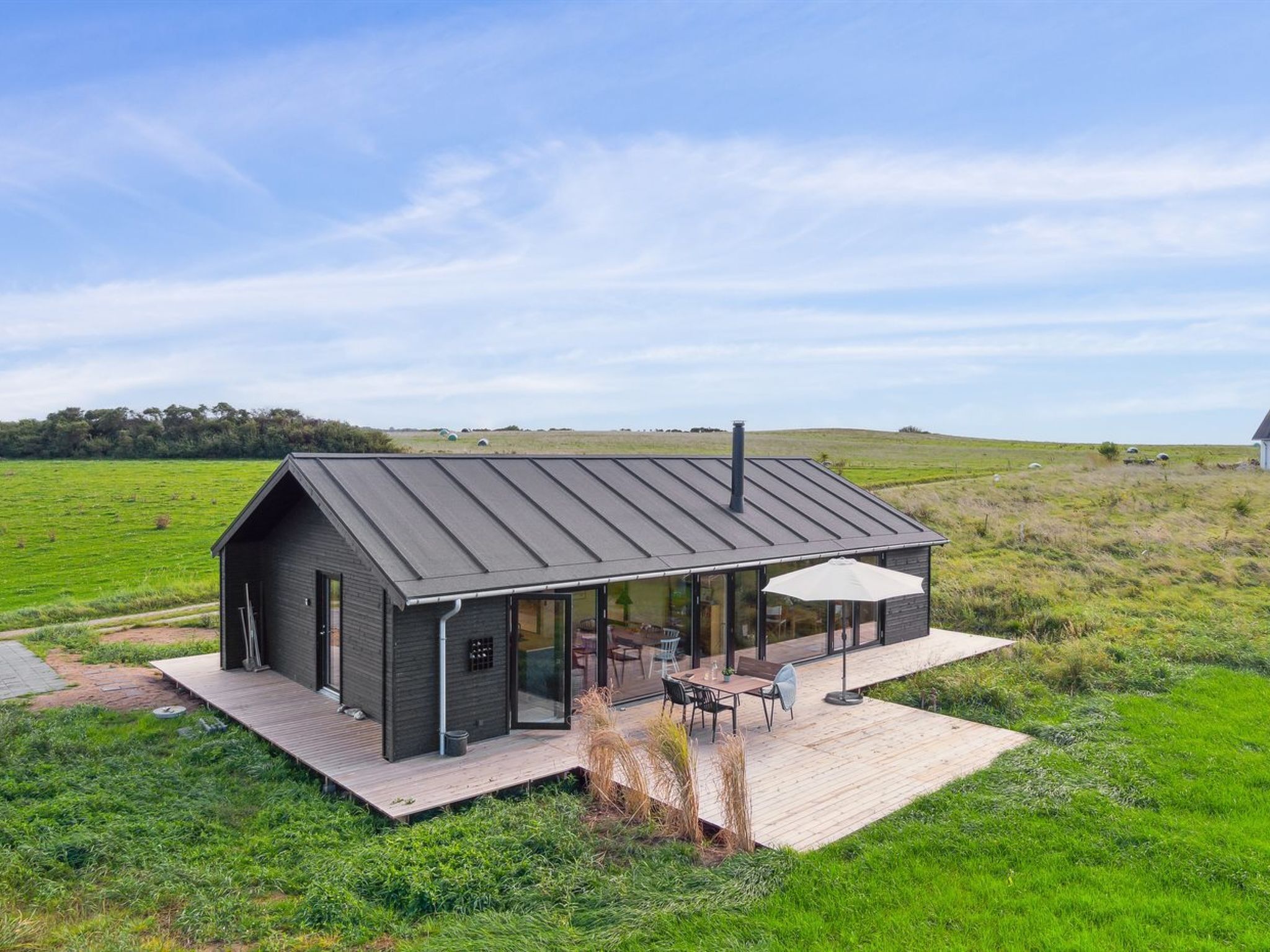 Ein modernes Haus mit einer großen Terrasse und Glastüren, umgeben von einer grünen Wiese.