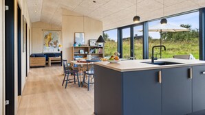 A modern kitchen with a large island, wooden chairs, a dining table, and a view of the outdoors. - "Aatos" - 250m from the sea by Interhome (Knebel)