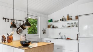 A modern kitchen with white cabinetry, a wooden island, hanging pots, and a window with a view of greenery.