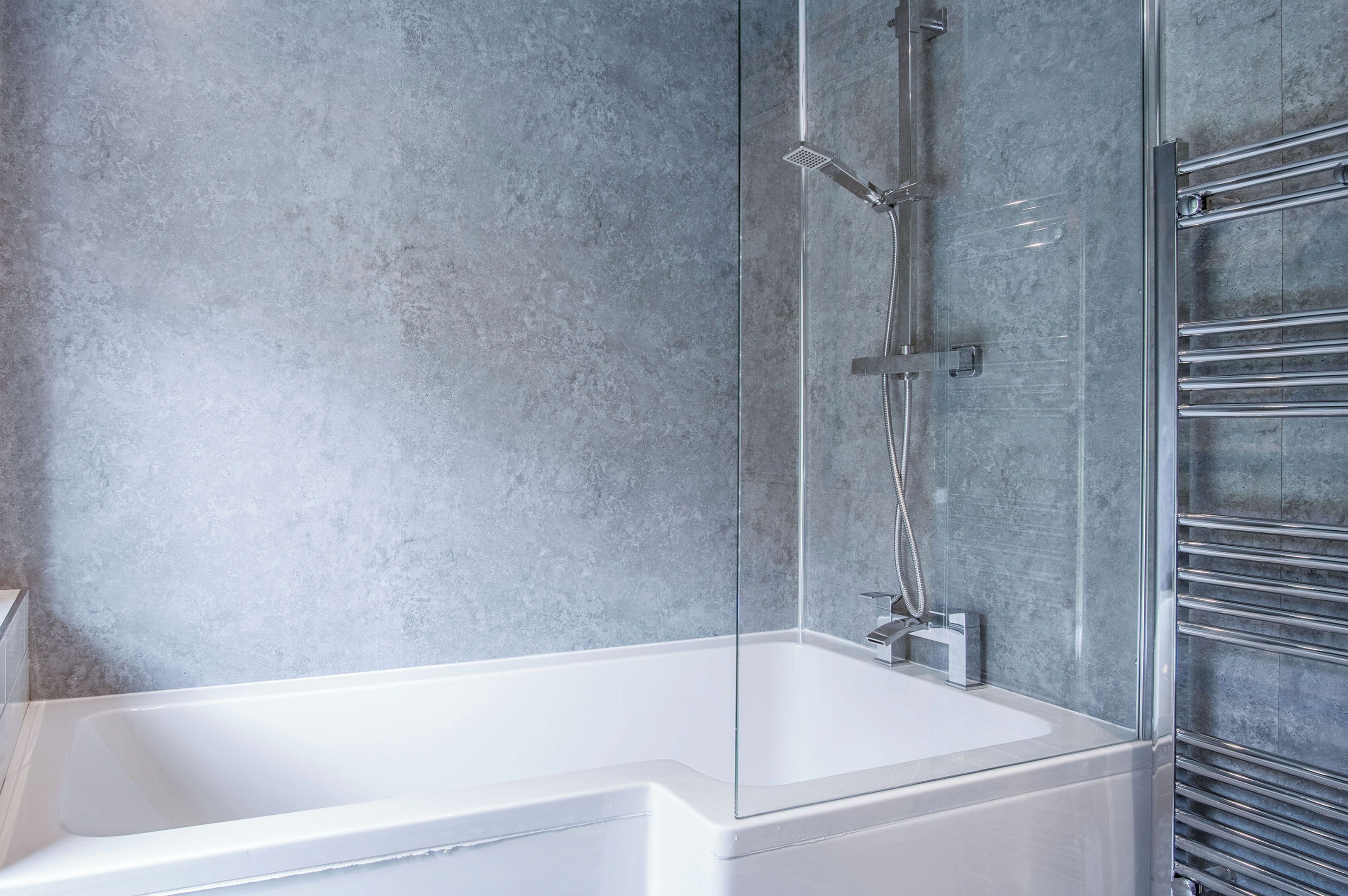 Ein modernes Badezimmer mit einer gläsernen Dusche, einer weißen Badewanne und einem chromfarbenen Handtuchhalter.