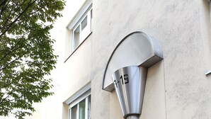 Een gevel met een moderne, metalen lamp, glazen deuren en een helder zicht op het interieur.