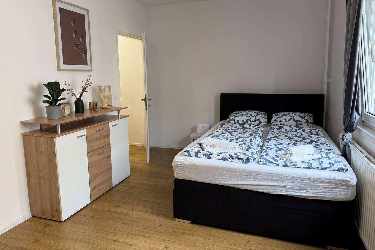 Un dormitorio con cama, mesita de noche, cómoda y un cuadro en la pared.