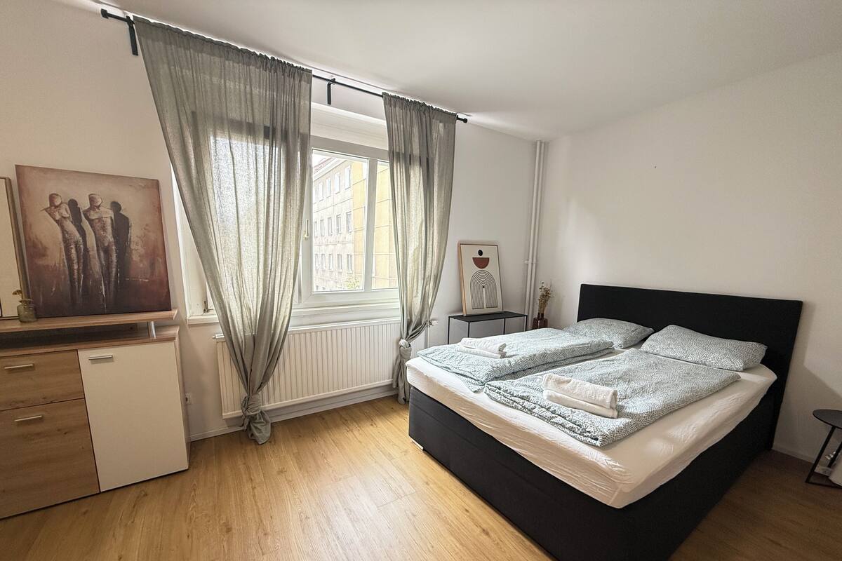 Un dormitorio con cama, cómoda, ventana con cortinas y un cuadro en la pared.