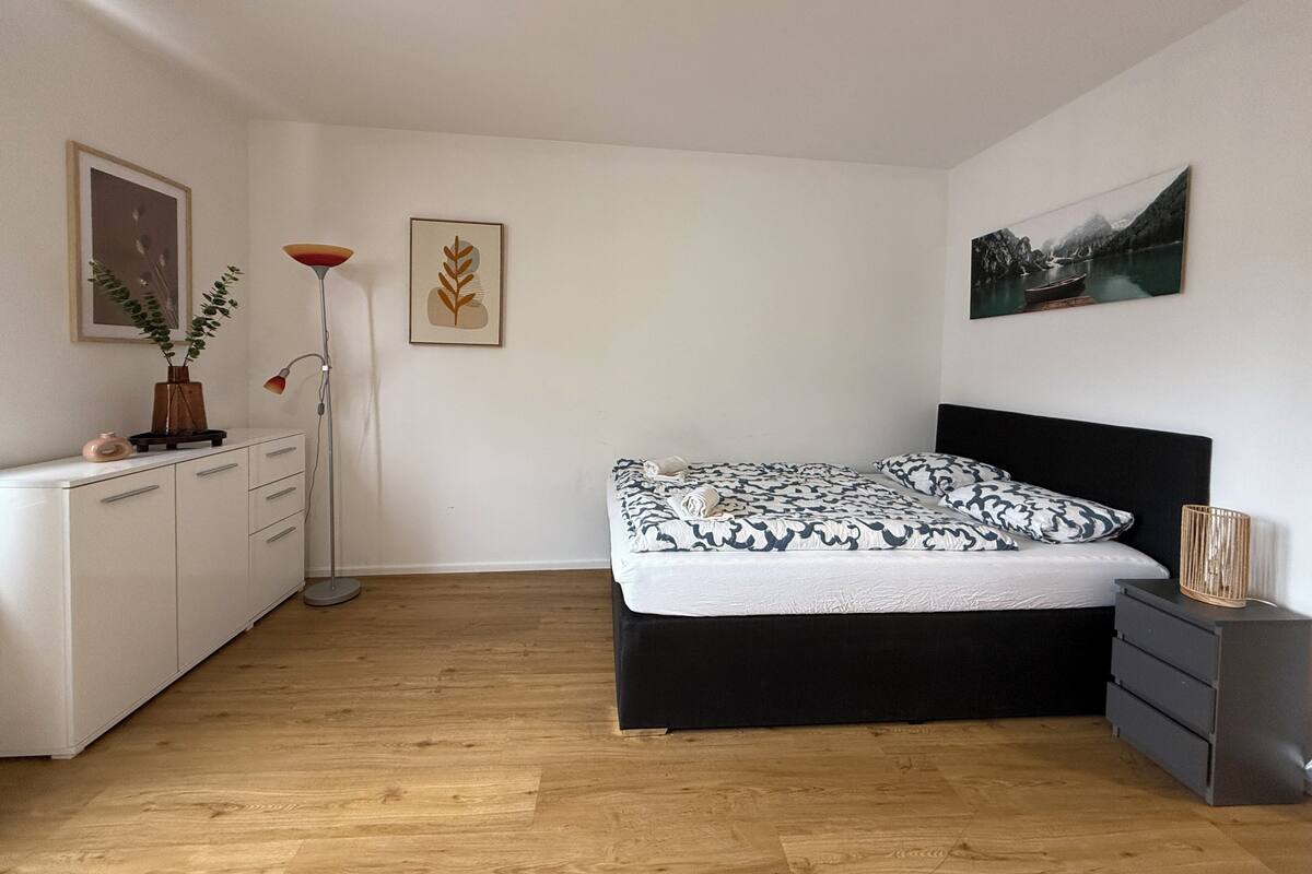 Un dormitorio con cama, mesitas de noche, cómoda, lámpara de pie y decoración en la pared.