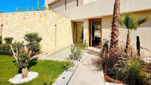 A modern house with a stone wall, a palm tree, and a small garden. - Palais Harmonia (Marrakech)