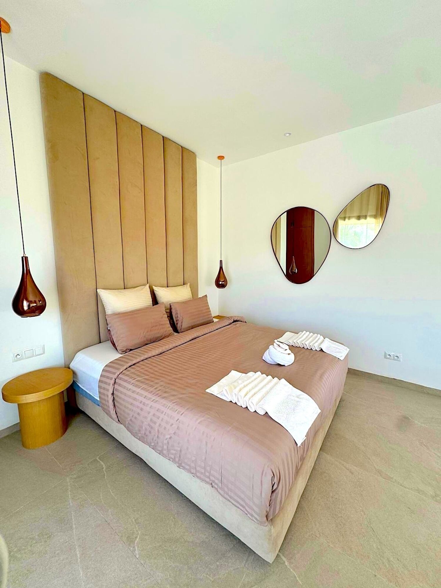 Une chambre à coucher moderne avec un grand lit, deux tables de chevet, une tête de lit en bois et deux miroirs fixés au mur.
