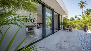 A modern outdoor living area with a glass-enclosed patio, a white bathtub, and lounge chairs. - Villa Manglar Luxury Oceanfront (Las Terrenas)