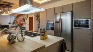 A modern kitchen with a stainless steel refrigerator, a built-in oven, and a central island with a vase and knife block. - Villa Manglar Luxury Oceanfront (Las Terrenas)