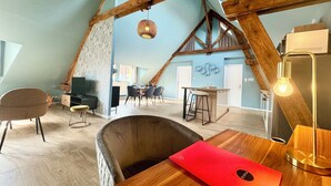 Un loft espacioso con vigas de madera a la vista, una zona de comedor y una acogedora sala de estar con una carpeta roja sobre una mesa.