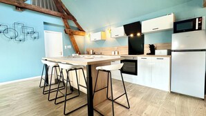 Cocina moderna con isla de madera, taburetes de bar, horno empotrado y refrigerador de acero inoxidable.