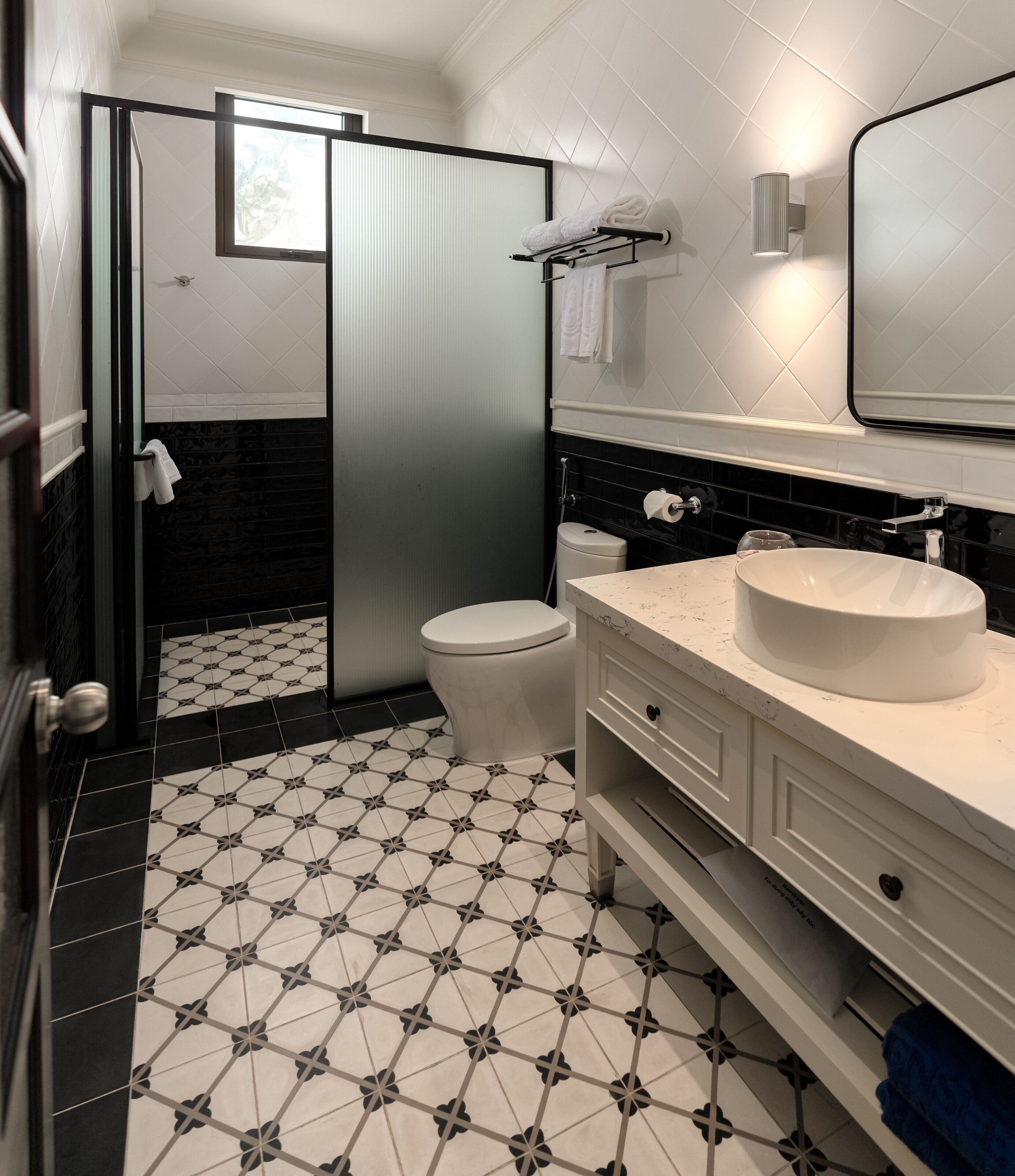 A modern bathroom with a black and white tiled floor, a white toilet, a large mirror, and a white sink with a marble countertop.