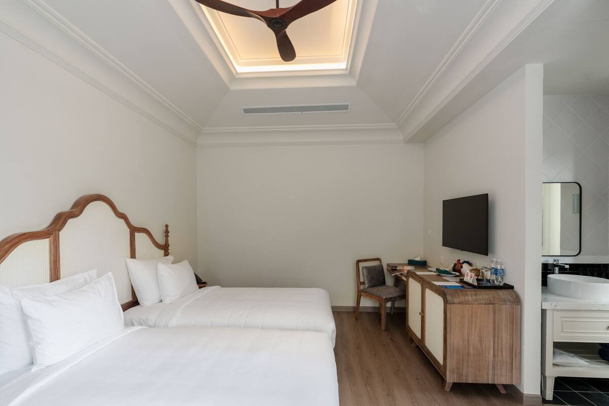 A hotel room with a bed, desk, chair, TV, and a bathroom with a sink and mirror.