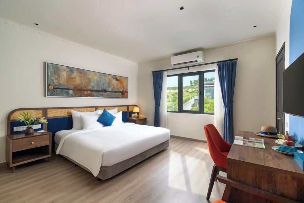 Une chambre d’hôtel avec un lit, une table de chevet, une lampe et une fenêtre avec des rideaux.