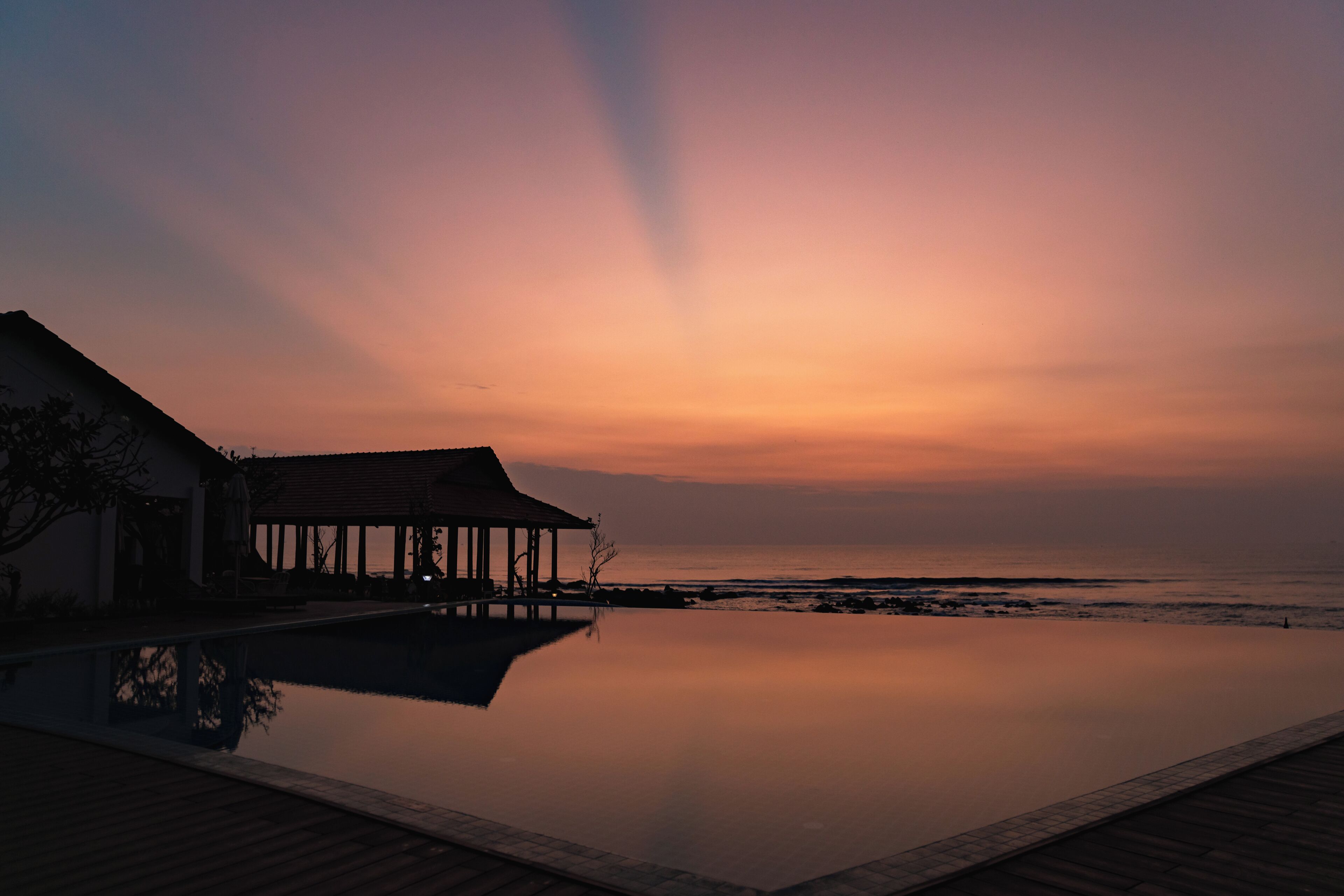 A serene sunset view over a calm pool with a wooden deck and a building with a covered patio.