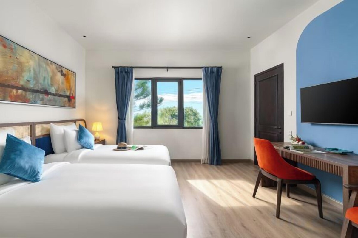 Habitación de hotel con dos camas, un escritorio, una silla, un televisor y una ventana con cortinas.