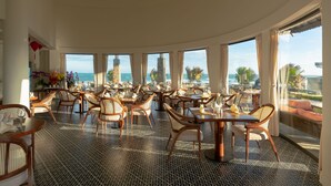 Ein Restaurant mit geschwungener Anordnung, großen Fenstern und Meerblick.