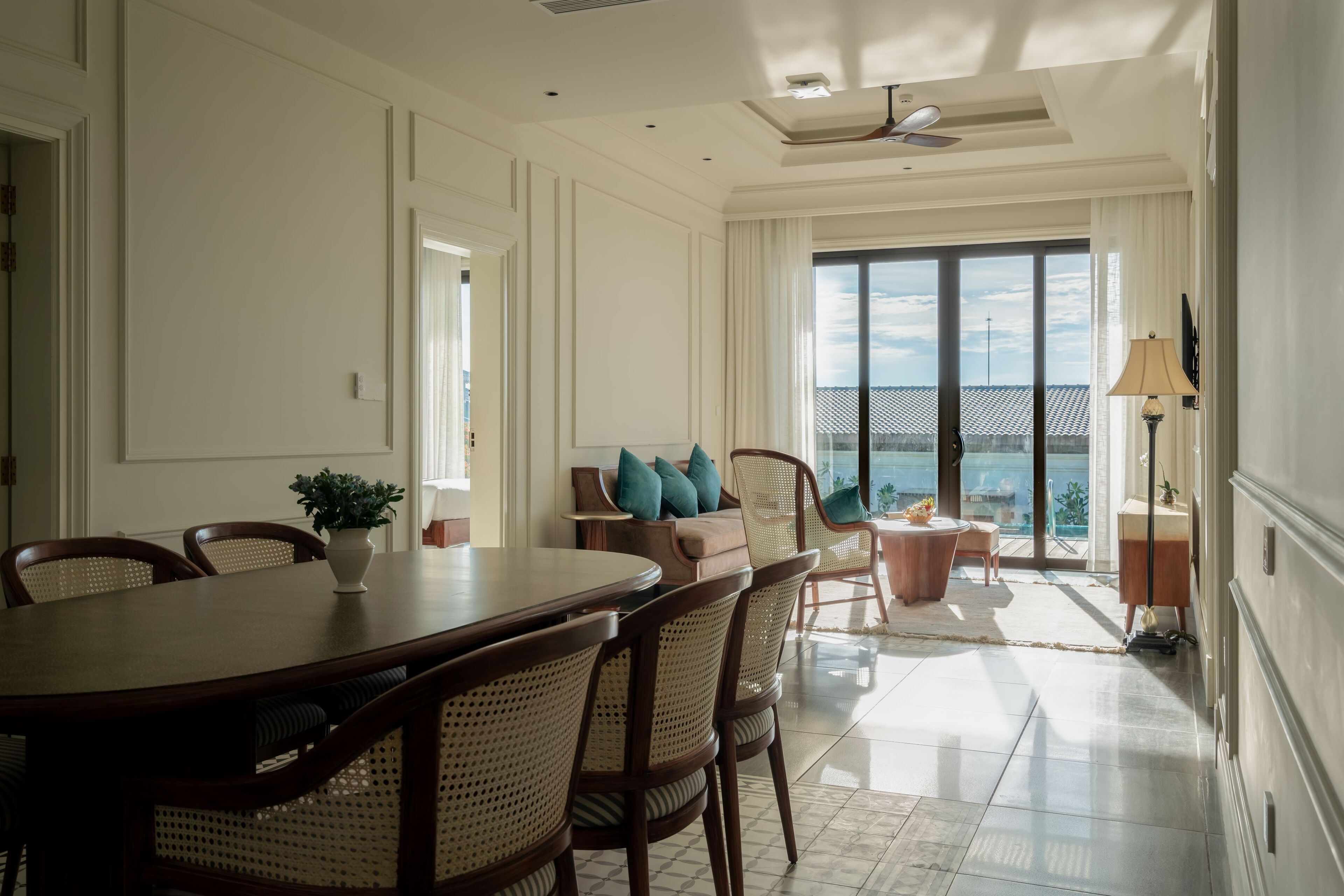 A spacious dining area with a large table and chairs, a sofa with cushions, and a view through a large window.