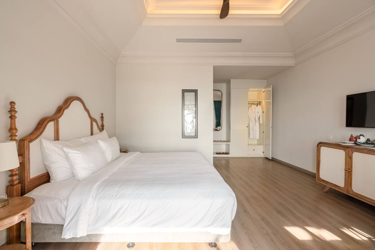 A spacious bedroom with a large bed, a wooden nightstand, a flat-screen TV, and a walk-in closet.