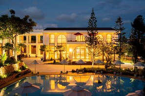 A hotel with a swimming pool, outdoor umbrellas, and a well-lit facade.