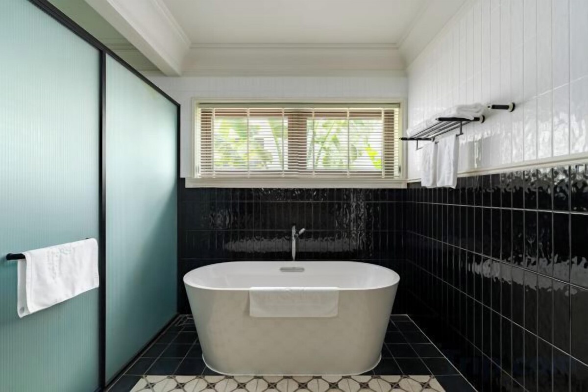 A bathroom with a freestanding bathtub, a window with blinds, and a towel rack.