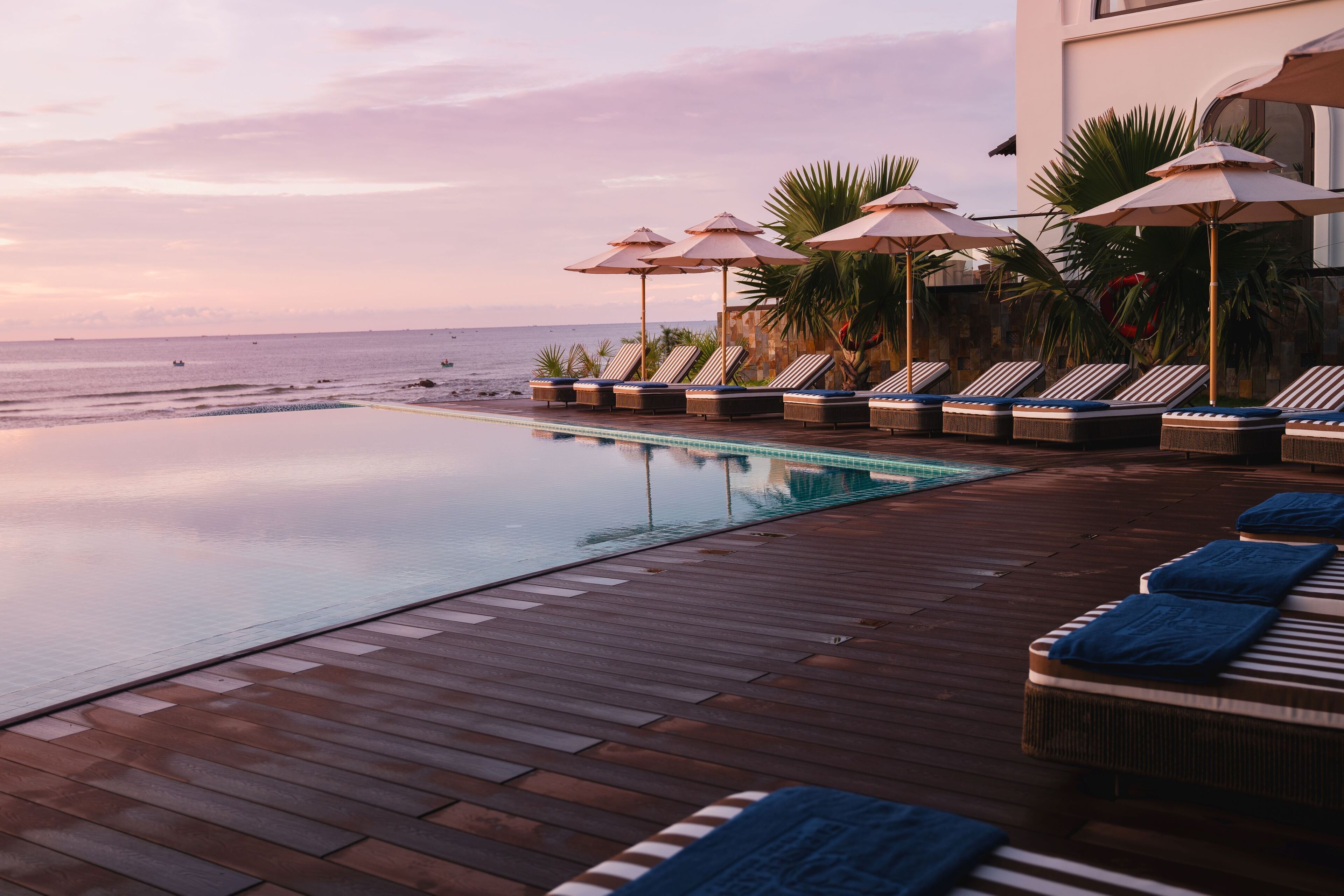 A wooden deck with lounge chairs and umbrellas overlooking a pool and the ocean.