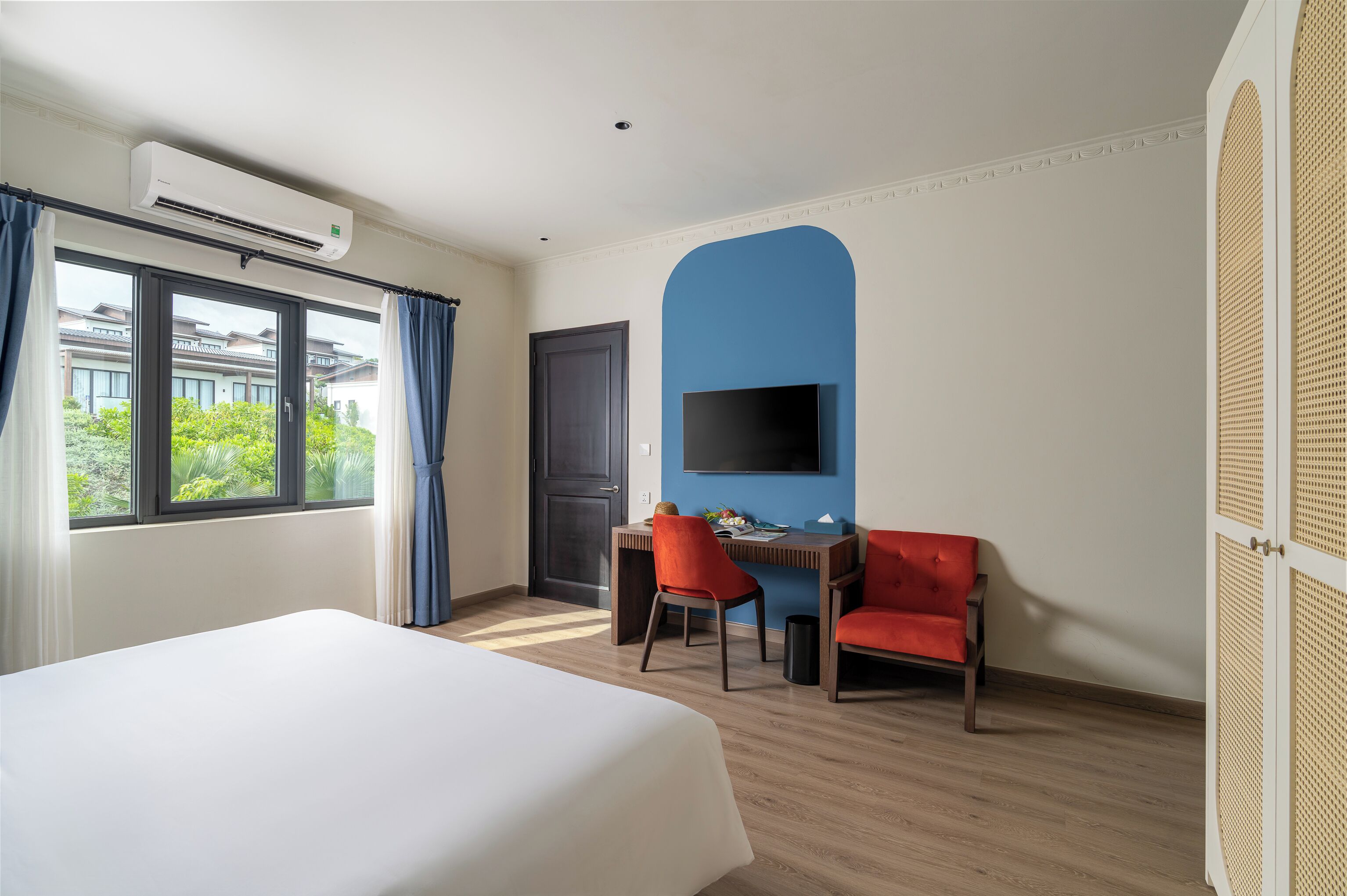 A hotel room with a bed, a desk with two chairs, a TV, and a window with curtains.