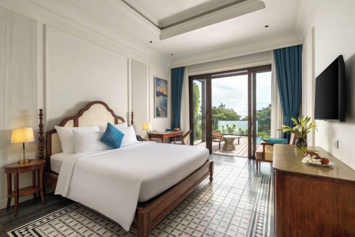 Une chambre d’hôtel avec un grand lit, un bureau, une chaise, une télévision et un balcon avec vue.
