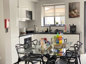 Una cocina moderna con armarios blancos, una mesa de comedor de vidrio, sillas negras y un ventanal con vistas al exterior.