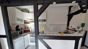 A kitchen with white cabinets, a stove, and a microwave. There are utensils and a green cup on the counter. - Cozy 2-room vacation apartment for 1-2 persons in Engelskirchen Loope (Engelskirchen)