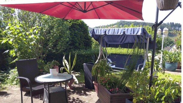 A patio with a table and chairs, a red umbrella, and potted plants. - Cozy 2-room vacation apartment for 1-2 persons in Engelskirchen Loope (Engelskirchen)