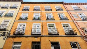 Un edificio de varios pisos con balcones, una puerta negra y un ventanal con persiana.